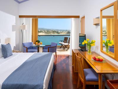 Hotelzimmer mit Bett, Schreibtisch und Blick auf Balkon mit Meerblick.