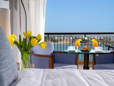 Hotelzimmer mit gelben Tulpen, Bett und Balkon mit Meerblick bei klarem Himmel.