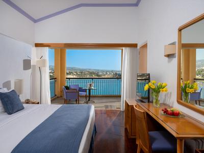 Helles Hotelzimmer mit Balkon und Blick auf das Meer und Stadt im Hintergrund.