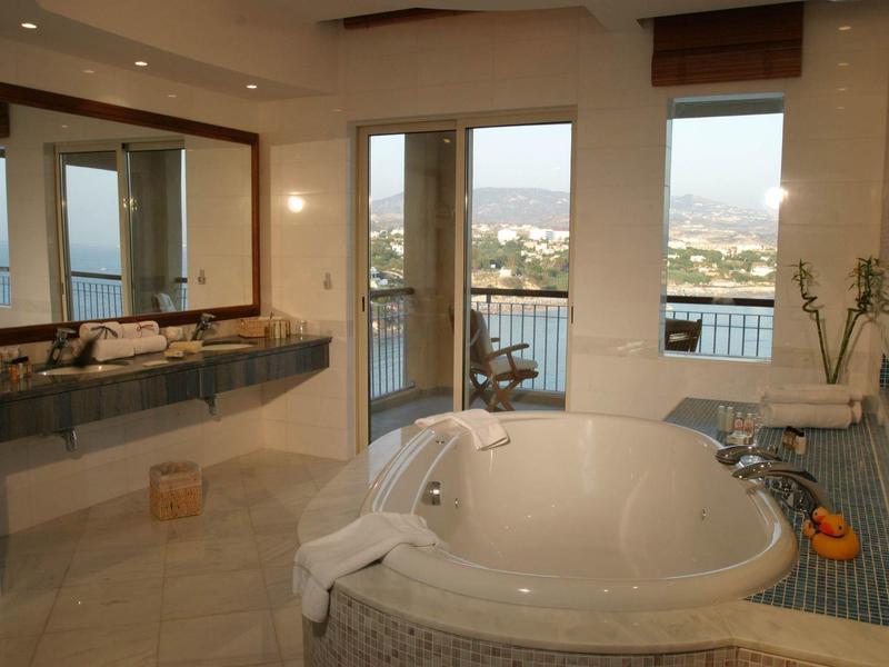 Großes Bad mit rundem weißen Whirlpool, Fenster mit Bergblick und grauen Fliesenboden.