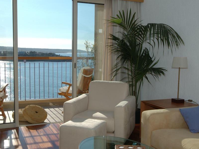 Wohnzimmer mit hellen Möbeln, Pflanzen und großer Glasschiebetür mit Meerblick und Balkon.