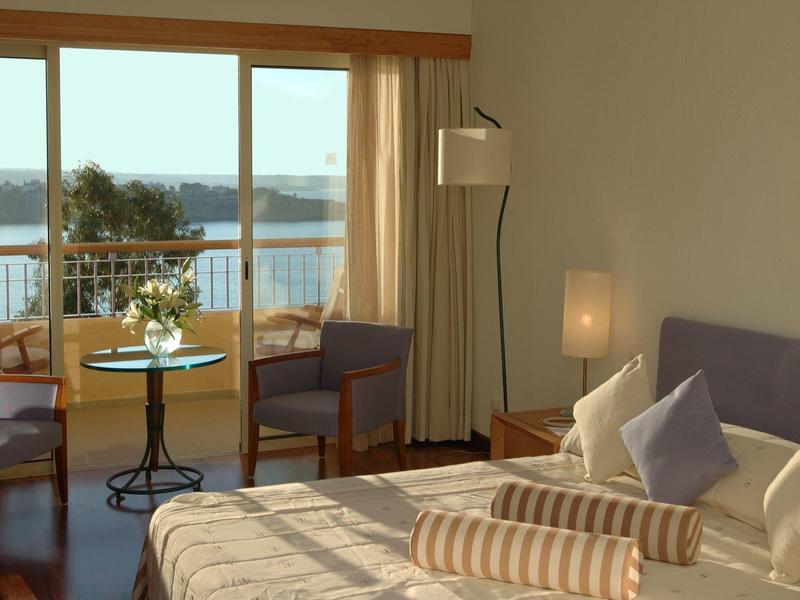 Gemütliches Schlafzimmer mit großem Bett, Sessel, Stehlampe und Balkon mit Meerblick.