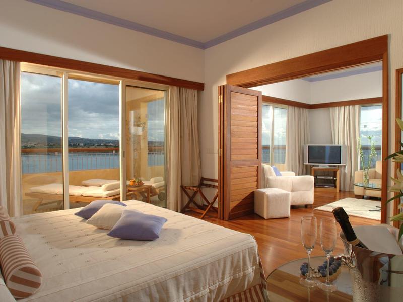 Helles Schlafzimmer mit Meerblick, großem Bett, Sesseln und Holzboden in warmen Tönen.