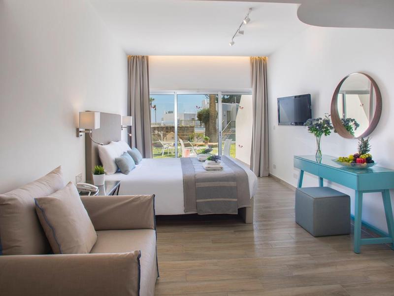 Helles Schlafzimmer mit großem Bett, Sofa, blauem Tisch, rundem Spiegel und Balkon mit Meerblick.