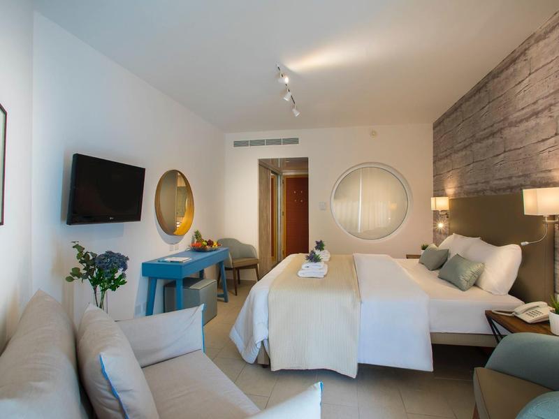 Modern eingerichtetes Hotelzimmer mit Doppelbett, Sofa, Wandspiegel und Fernseher.