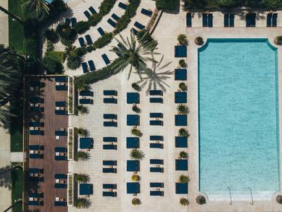 Vogelperspektive eines rechteckigen Pools mit Liegestühlen und Palmen in einem Hotelresort.