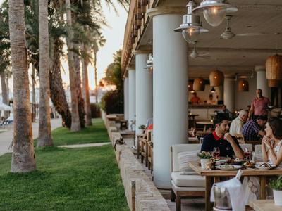 Gemütliches Restaurant mit Außenbereich neben Palmen und Grünfläche bei Sonnenuntergang.