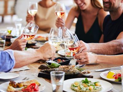 Menschen stoßen mit Weingläsern bei einem Restaurantessen an.