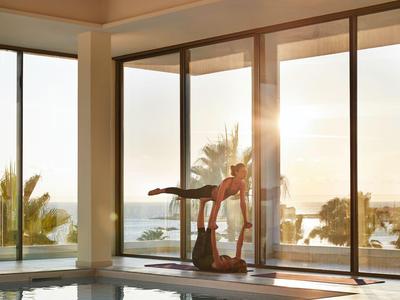 Moderner Innenpool mit großen Fensterfronten und Ausblick auf Palmen und Sonnenuntergang.