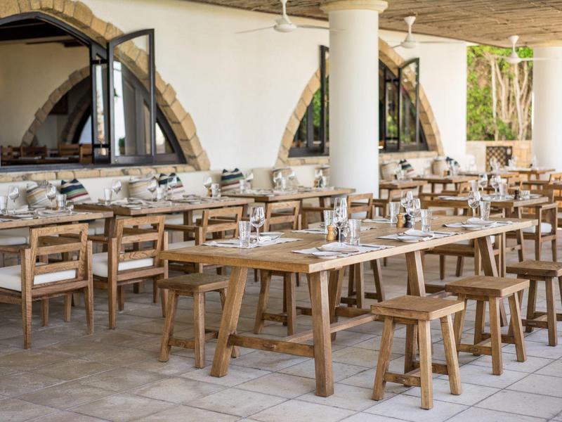 Freiluftrestaurant mit Holztischen und -stühlen, großen Fenstern und mediterranem Flair.