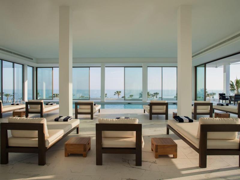 Moderner, offener Wohnraum mit großen Glasfenstern, Holzmöbeln und Blick auf Pool und Meer.