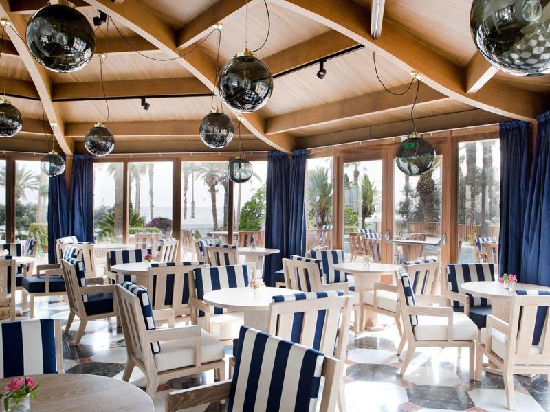 Helles Café mit Holzdecken, großen Fenstern und blauen, gestreiften Stühlen.