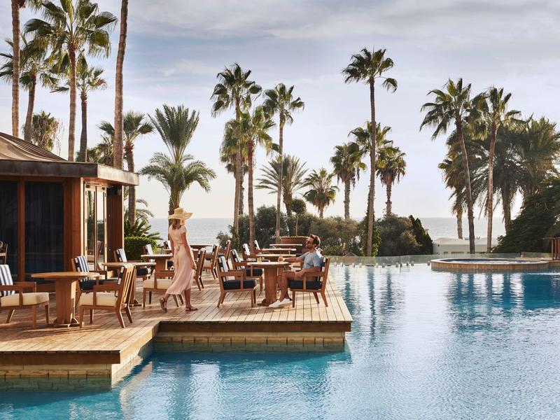 Einladender Pool mit klarem Wasser, Palmen und Menschen unter blauem Himmel am Resort.