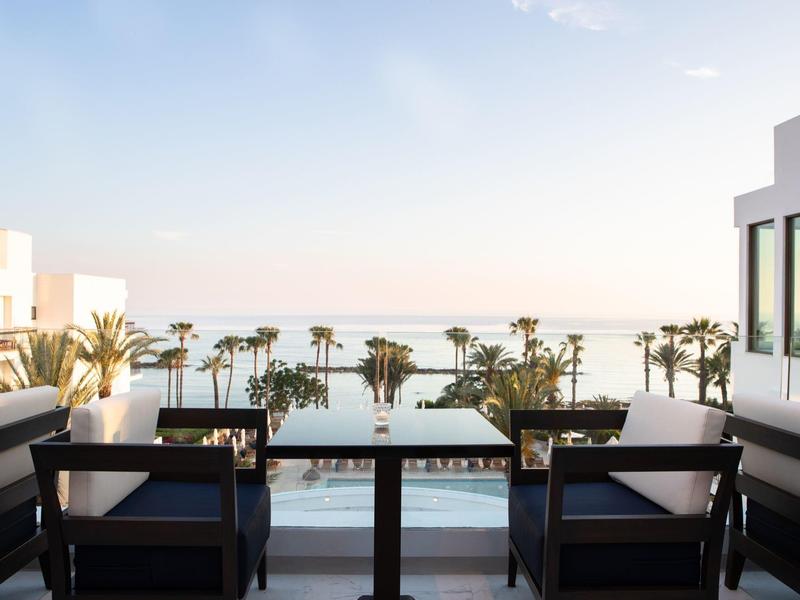 Balkon mit schwarzem Tisch und Stühlen, Blick auf Palmen und das Meer bei klarem Himmel.