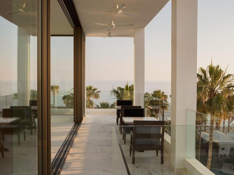 Moderner Balkon mit schwarzen Stühlen, Glasgeländer und Meerblick bei Sonnenuntergang.