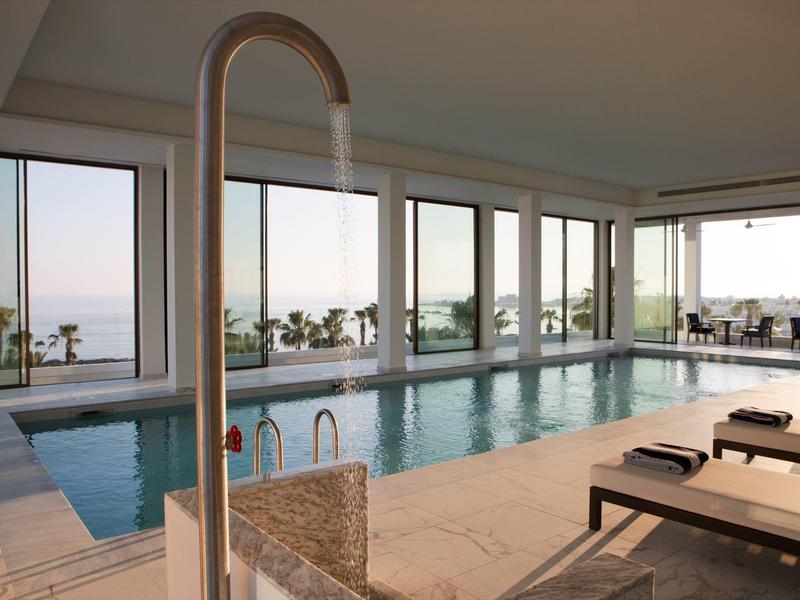 Moderner Indoor-Pool mit Glasfront, Liegestühlen und Blick auf Garten und Meer.