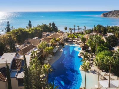 Blick auf ein Resort mit großem Pool, Palmen und direktem Zugang zum blauen Meer bei Sonnenschein.