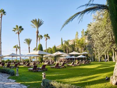 Jardin vert avec chaises longues et parasols sous des palmiers par ciel clair
