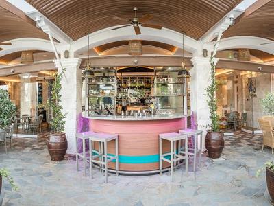 Bar ouverte avec comptoir rose et tabourets colorés dans un restaurant d'hôtel avec arcs en bois.