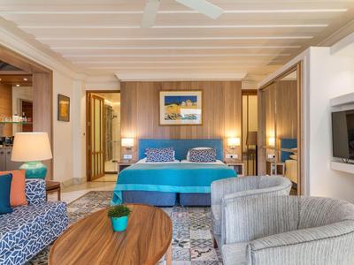 Modern eingerichtetes Schlafzimmer mit großem Bett, hellem Holz, Sitzbereich und farbigen Akzenten.