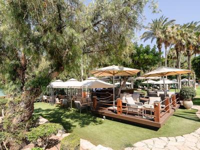 Restaurant en plein air avec plancher en bois, tables blanches et parasols à côté d'arbres et plantes vertes