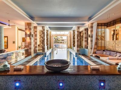 Moderner Innenpool mit Holzbeckenrand, Glaswänden und warmem, einladendem Licht.