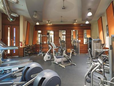 Salle de sport lumineuse avec divers appareils d'exercice et grandes fenêtres avec rideaux orange.