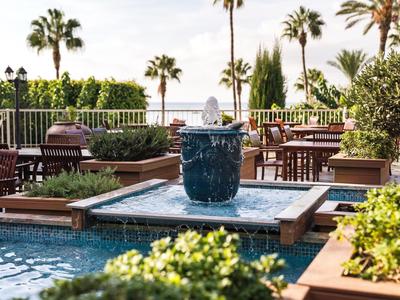 Terrasse d'hôtel avec fontaine, plantes et espaces de détente au soleil.