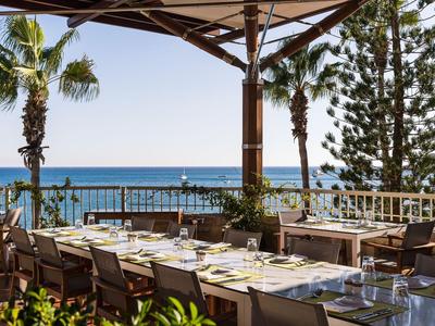 Terrasse avec tables dressées donnant sur la mer et des palmiers en arrière-plan.