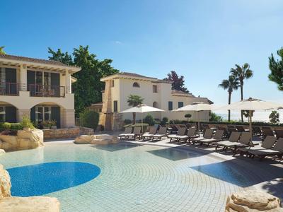 Großer Pool mit blauer Wasserfläche, Liegestühlen, Sonnenschirmen und mediterranen Gebäuden.