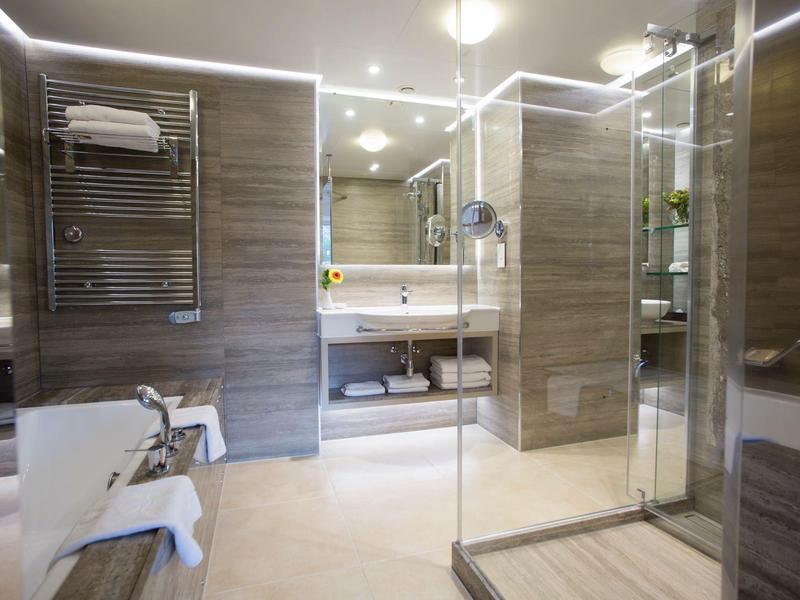 Modernes Badezimmer mit Glas-Dusche, Holzfliesen, weißen Sanitäranlagen und beleuchtetem Spiegel.