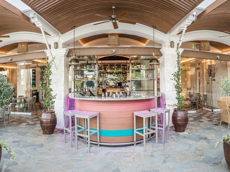 Gemütliche Terrasse mit Holzbalkendecke, buntem Tresen und mehreren Sitzgruppen aus Holz und Metall.