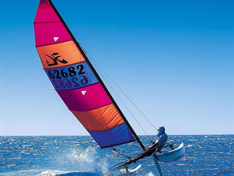 Ein Segelboot mit buntem Segel fährt schnell über das blaue Meer bei klarem Himmel.