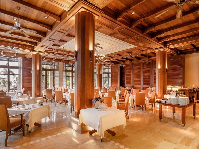 Großer, eleganter Speisesaal mit Holzbalkendecke, weißen Tischdecken und hellbraunen Stühlen.