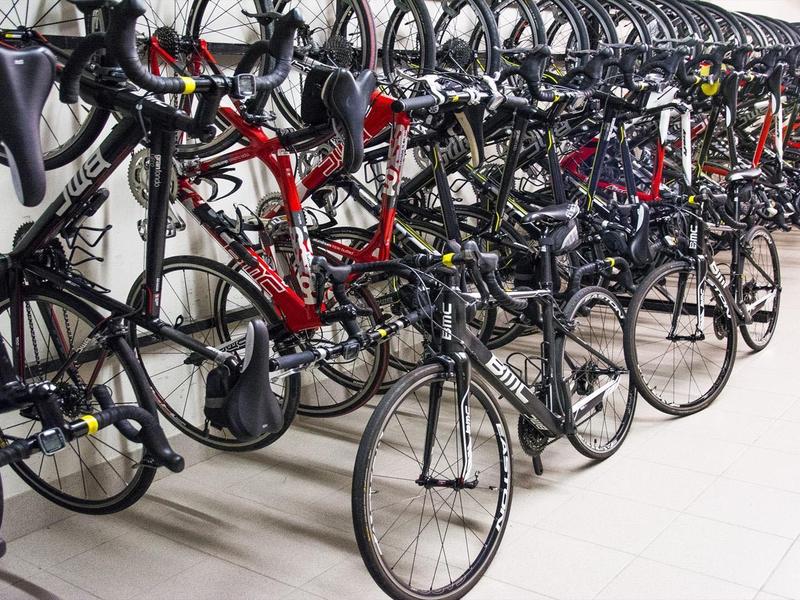 Viele Rennräder in verschiedenen Farben stehen dicht in einer modernen, gut beleuchteten Halle.