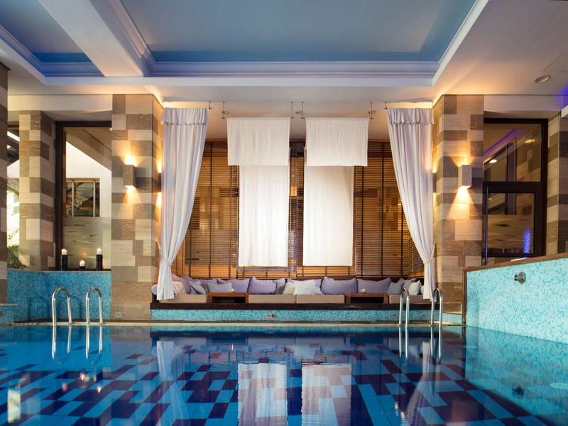 Innenpool mit blauen Fliesen, Glaswänden, weißen Vorhängen und warmem Licht in modernem Raum.