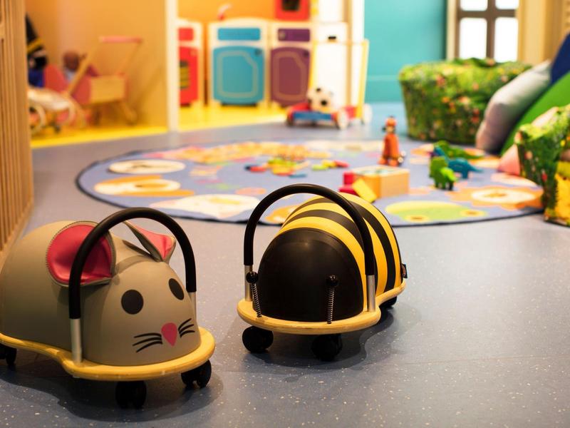 Zwei bunte Kinderkoffer in Form einer Maus und einer Biene auf blauem Boden in einem Spielzimmer.