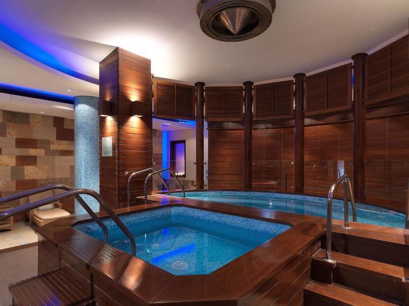 Innenraum mit blau beleuchtetem Whirlpool, hölzernen Wänden und modernen Deckenleuchten.