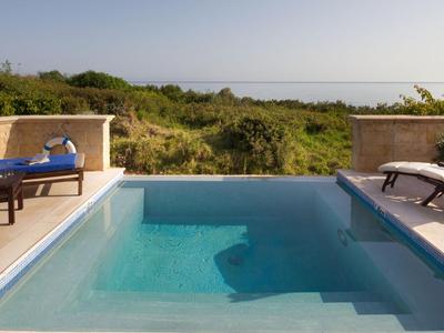 Pool mit klarem Wasser und Sonnenliegen mit Blick auf grüne Landschaft und Meer im Hintergrund.