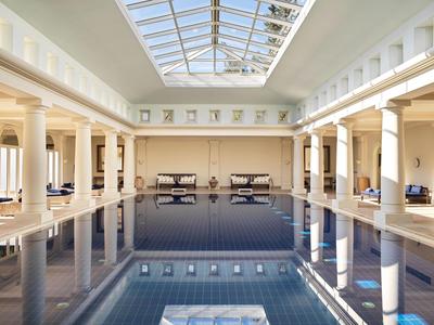 Helles Hotelhallenbad mit Säulen und großen Fenstern unter einem Glasdach.