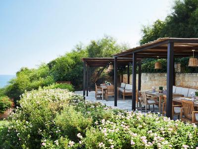 Offener Pavillon mit Essbereich, umgeben von grüner Vegetation und Blick auf das Meer.