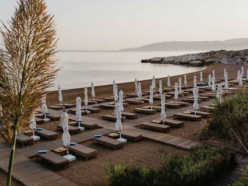 Strand mit geordneten Liegen und geschlossenen Sonnenschirmen am ruhigen Meer bei Dämmerung.