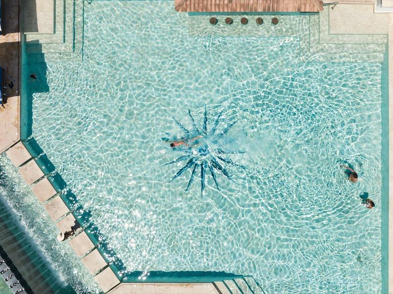 Großes Freibad mit klarem Wasser, Springbrunnen in der Mitte und zwei Schwimmern rechts.