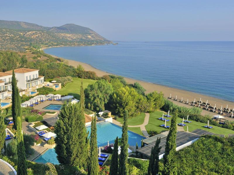 Landschaft mit Hotelpool, grünen Bäumen, Sandstrand und blauem Meer unter klarem Himmel.