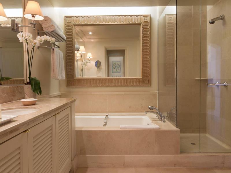 Helles Badezimmer mit großer Badewanne, Glasdusche, schwarzem Spiegel und Orchideen auf der Arbeitsplatte.