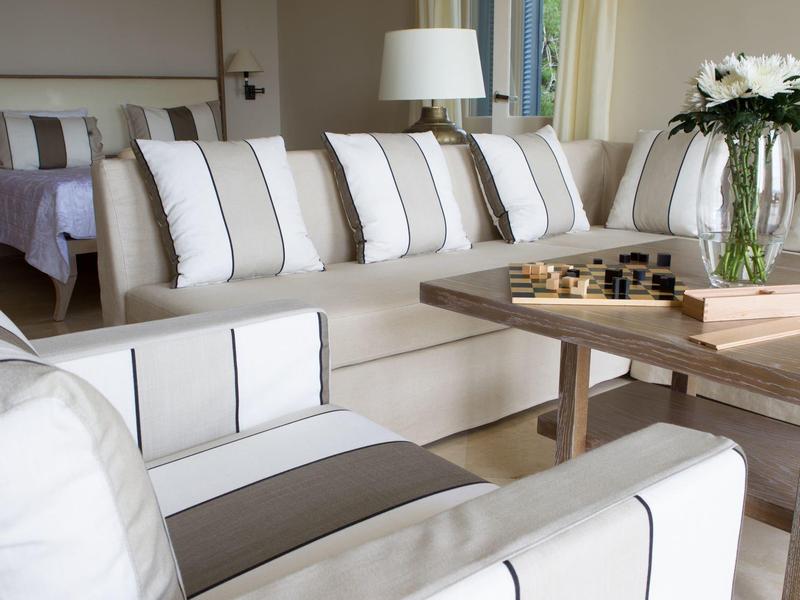 Helles Wohnzimmer mit weißem Sofa, gestreiften Kissen, Holztisch und Blumen auf der Fensterbank.