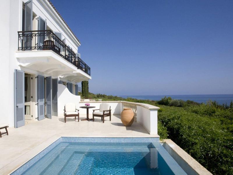 Moderner weißer Balkon mit Pool und Holzmöbeln, grüner Landschaft und blauem Himmel im Hintergrund.