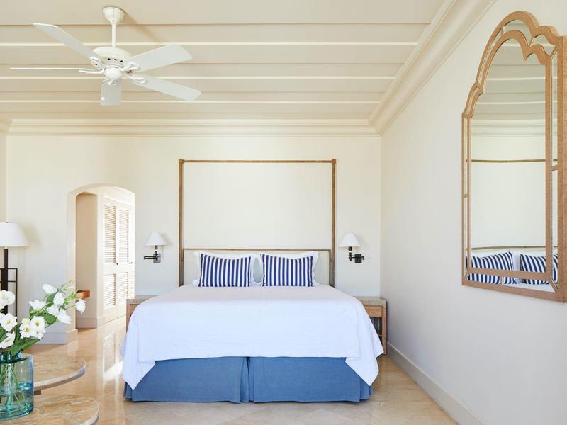 Hell eingerichtetes Schlafzimmer mit Doppelbett, blau-weißer Bettwäsche, großem Spiegel und Deckenventilator.