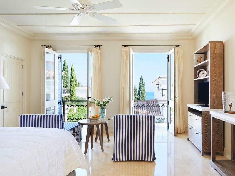 Helles Schlafzimmer mit Meerblick, zwei Sesseln, Holzmöbeln und weißen Wänden.