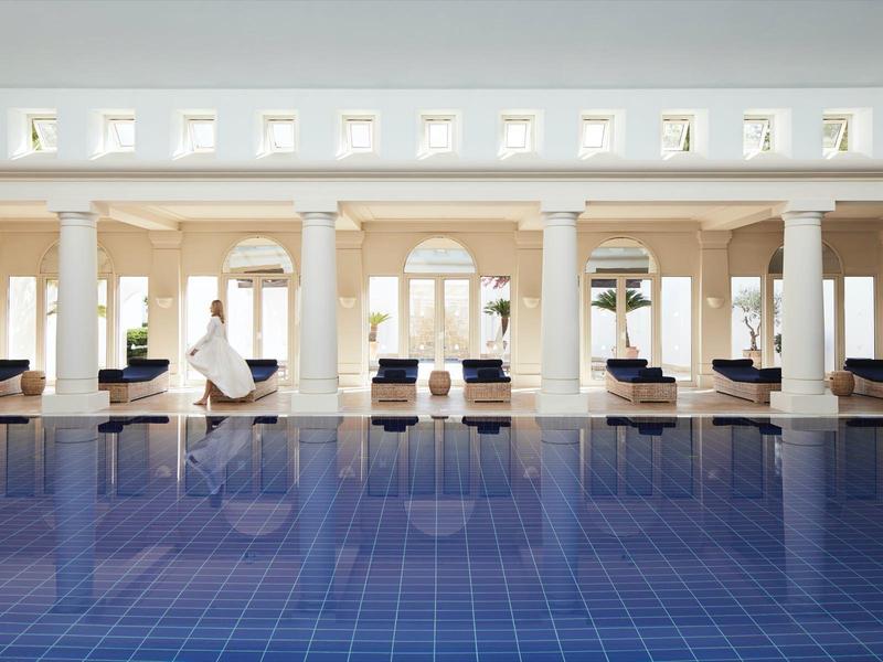 Ein großer Innenpool mit blauen Fliesen, umgeben von weißen Säulen und Loungesesseln.